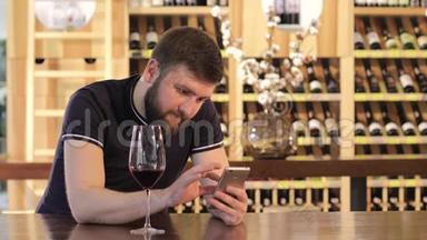 一个年轻人在喝红酒时使用智能手机，一个孤独的男人拿着一杯红酒，一个穿着一件衣服的年轻人